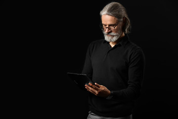 Handsome mature businessman with tablet computer on dark background