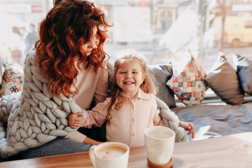 Inside portrait of young mother with little  daughter enjoying of good sunny day in cafeteria and drinking a cacao