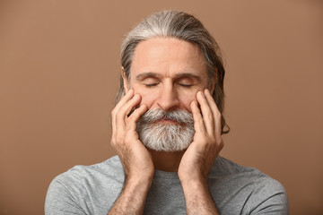 Portrait of mature man touching his face on color background