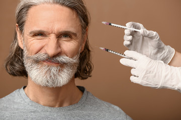 Mature man and hands holding syringes for anti-aging injections on color background
