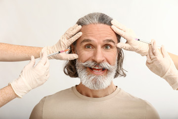 Mature man and hands holding syringes for anti-aging injections on white background