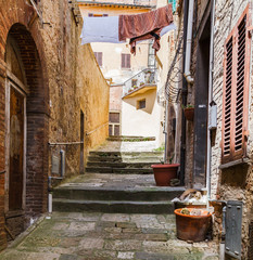 Fototapeta na wymiar Picturesque narrow street in ancient medieval hills town of Montepulciano, linen hanging between the old houses, fat cat lying on the stones. Tuscany, Italy.