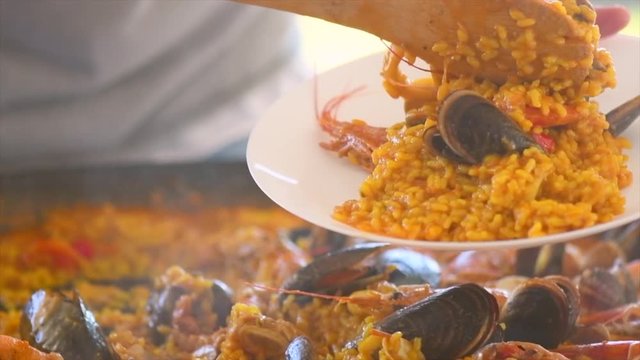 Paella traditional Spanish food. Person putts seafood paella from the fry pan to plate. Paella with with mussels, king prawns, langoustine and squids. Slow motion 4K UHD video footage. 3840X2160