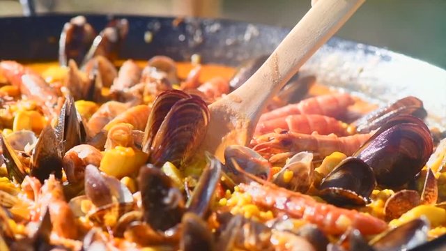 Paella. Person cooking traditional spanish seafood paella with prawns, mussels and fish closeup. Slow motion 4K UHD video footage. 3840X2160