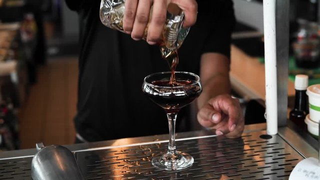 Black Manhattan being poured into a glass in slow motion. Rich brown tones are found in this shot from the natural light that this location had to offer