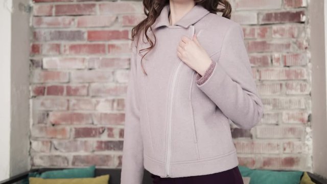 the girl fastens a zipper coat of grey color. close-up.