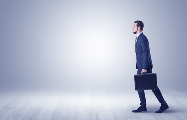 Successful businessman walking in front of an empty wall with briefcase on his hand
