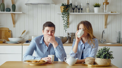 sad couple blonde girl and guy have breakfast drinking tea with biscuits silently and man yawns at...