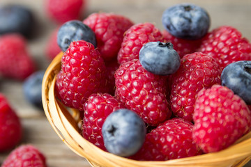 Raspberries and blueberries in a basket on a wooden table.