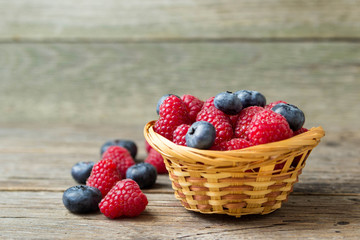Raspberries and blueberries in a basket on a wooden table.