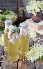 Elderflower cordial syrup and blossom flower in wooden background. Edible elderberry flowers add...