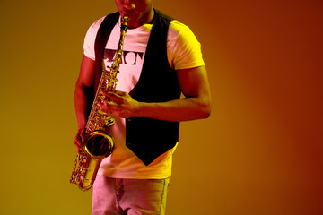 African American handsome jazz musician playing the saxophone in the studio on a neon background....