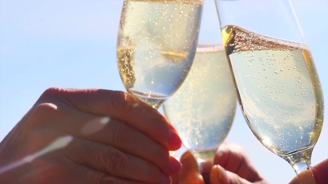 People holding Glass of sparkling Wine, Making a toast over Sunset sky and sea. Birthday. Group of Friends celebrating, drinking Wine, toasting. Party outdoors. Enjoying time together. Slow motion 4K
