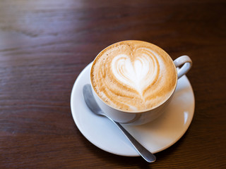 One cup of cappuccino with latte art on wooden table, white ceramic cup, place for text. Cafe culture.
