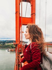 A girl with long hair in a red jacket hangs from the Golden gate bridge in San Francisco