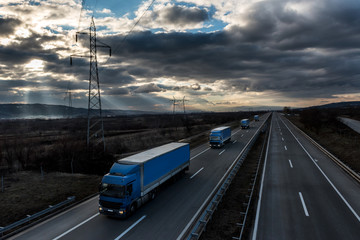 Caravan or convoy of lorry trucks on country highway under a dramatic sky