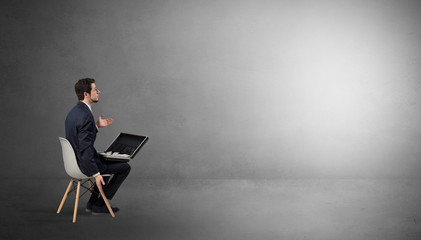 Businessman staying in an empty grey dark room with stuffs on his lap
