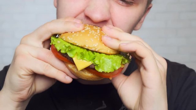 young man bites and eats Fastfood. Close-up. Cheeseburger, hamburger, sandwich.