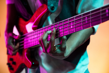 Obraz premium African American handsome jazz musician playing bass guitar in the studio on a neon background. Music concept. Young joyful attractive guy improvising. Close-up retro portrait.