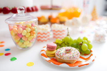 food and festive concept - grapes, macarons and donut on party table