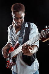 African American handsome jazz musician playing bass guitar in the studio on a black background. Music concept. Young joyful attractive guy improvising. Close-up retro portrait.