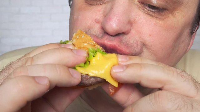 Adult man eating a nourishing hamburger. Junk food. Close-up.