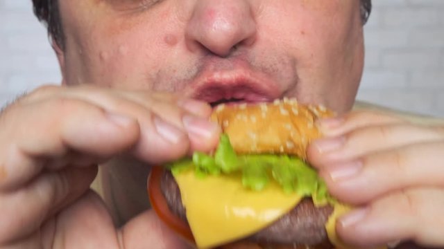 Adult man eating a nourishing hamburger. Junk food. Close-up.