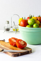 Tomatoes on board with bowl of tomatoes in background