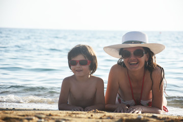 Mother and son enjoying on sandy beach. Happy woman with hat and little son relax on sea on summer vacation