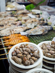 Close-up babylonia snail in paper dish and blured fishes, squids, seafood.