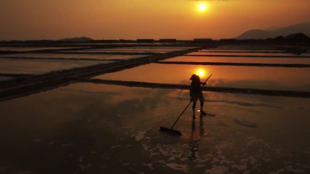 Worker silhouetted against the golden evening sun raking the salt fields