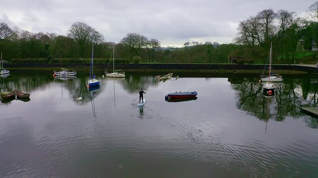 Beautiful aerial view, footage of middle aged man paddle boarding on Rudyard Lake in the Derbyshire Peak District National Park, popular holiday, tourist location with peaceful calm water