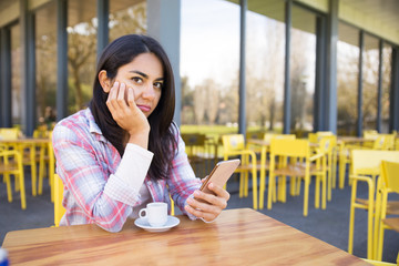 Serious woman sitting in street cafe with smartphone and coffee