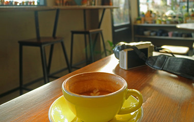 Half cup of cappuccino coffee on a wooden table with a white camera during break time