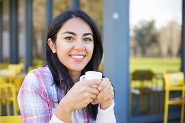 Smiling pretty young woman enjoying drinking coffee in cafe