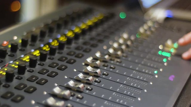 Recording studio digital audio mixer faders and sliders being operated by hand w/ depth of field and soft background focus.