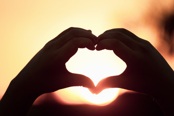 Fototapeta premium Beautiful Silhouette hand made heart shape on the sunset background.