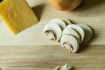 sliced ​​champignons with cheese on a kitchen board on wooden background