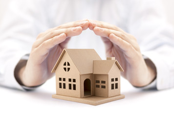 Property insurance. House miniature covered by hands. 