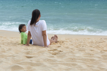Mother and toddler sitting on the beach watching the ocean.