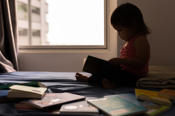 A little girl reading a book on her bed. 