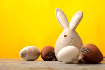 On a wooden surface there is an easter jolly rabbit and brown and white eggs, a yellow background. Cropped shot, horizontal, free space for text, side view. Easter concept.