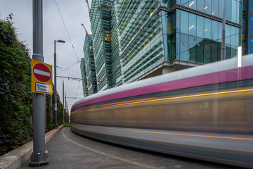 A tram in Birmingham, England. The tram is moving past modern, glass fronted office buildings  - obrazy, fototapety, plakaty