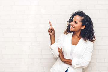 Smiling african american black woman pointing to empty copy space standing on white brick wall...
