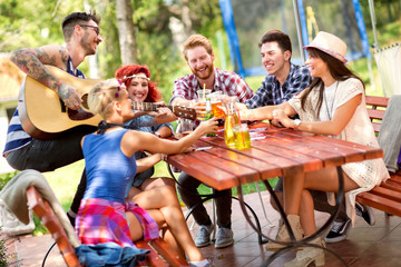 Smiling people tapping with glasses of beer while tattooed guy play guitar