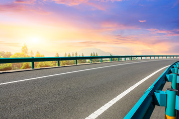 Asphalt highway and forest with mountain scenery at sunset