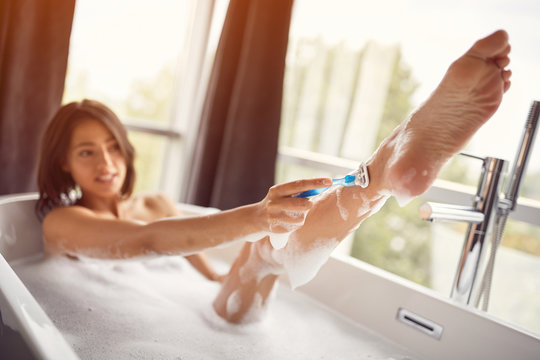 woman shaving legs in bathroom - depilation with razor.
