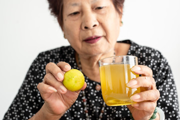 Asian senior woman holding lemon and honey juice in glass at home, lifestyle concept.