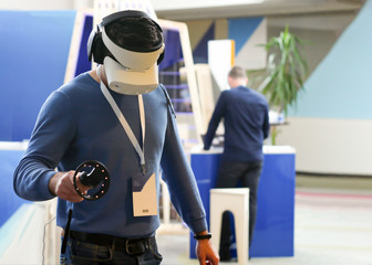 the person at the exhibition tries virtual reality in 3D glasses, headphones and a remote control