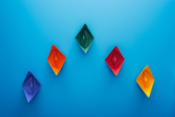 Flat lay with colorful paper boats on blue surface